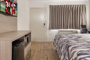 A hotel room with a bed, a TV mounted on the wall, a door, a window with curtains, and a small desk with a chair. - Red Roof Inn Fort Worth South (Fort Worth)