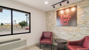 Red Roof Inn -hotellin sisätilat: kiviseinä, kaksi punaista tuolia, pieni pöytä ja suuri ikkuna, josta on näkymä ulos.