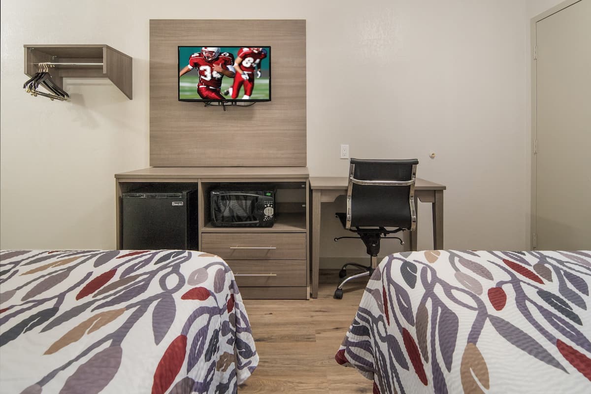 A hotel room with two beds, a desk with a chair, a television mounted on the wall, a microwave, and a small storage cabinet.