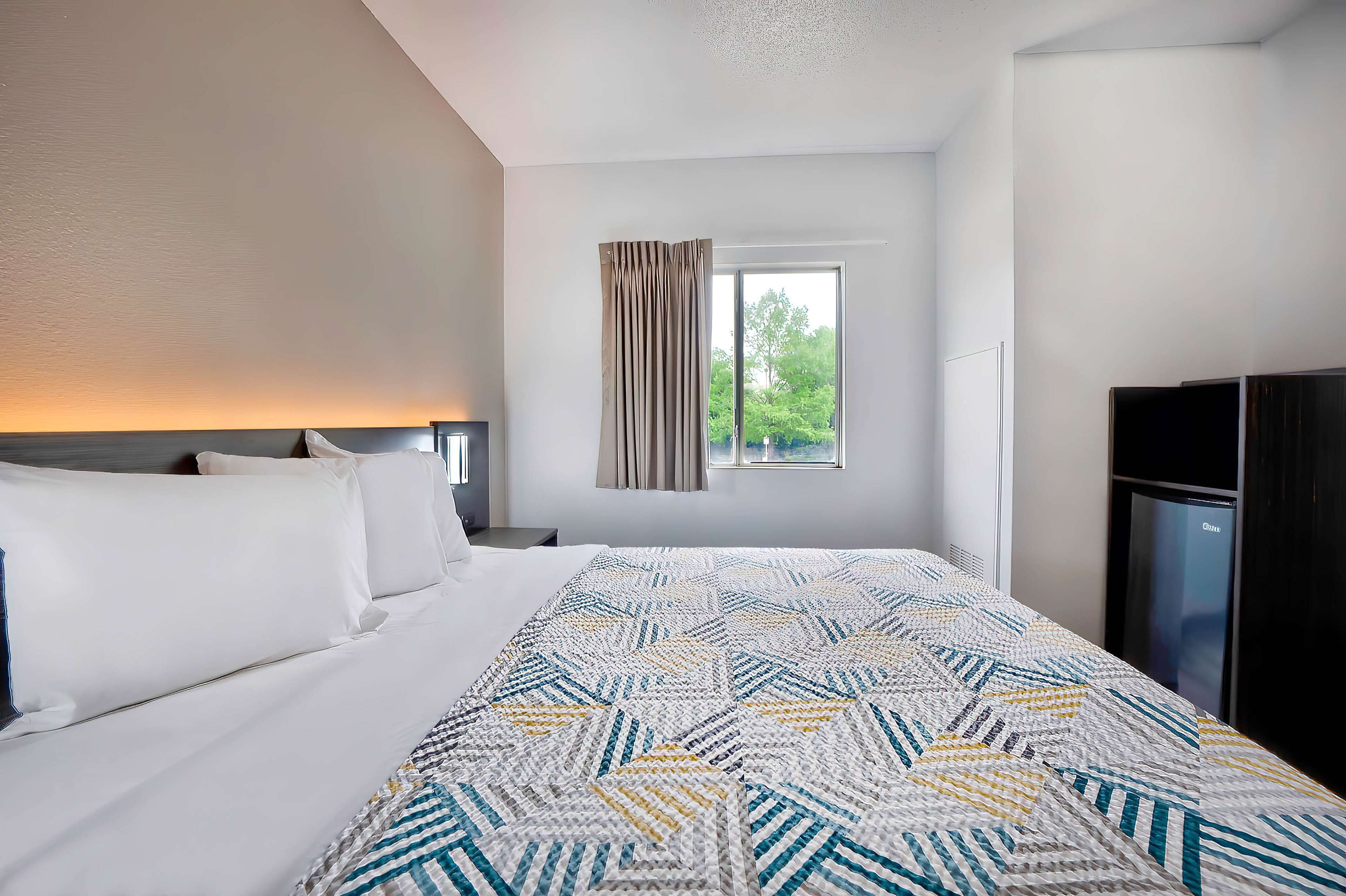 Habitación de hotel con una cama grande, una ventana con cortinas, un televisor y un minibar.