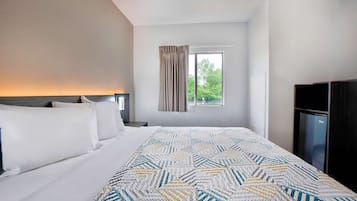 Habitación de hotel con una cama grande, una ventana con cortinas, un televisor y un minibar.