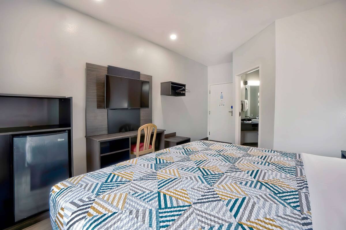 A hotel room with a bed, a desk, a chair, a TV, and a wardrobe.