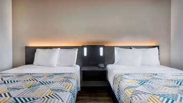 A hotel room with two beds, each with a patterned bedspread, a bedside table with a phone, and a wall-mounted light fixture.