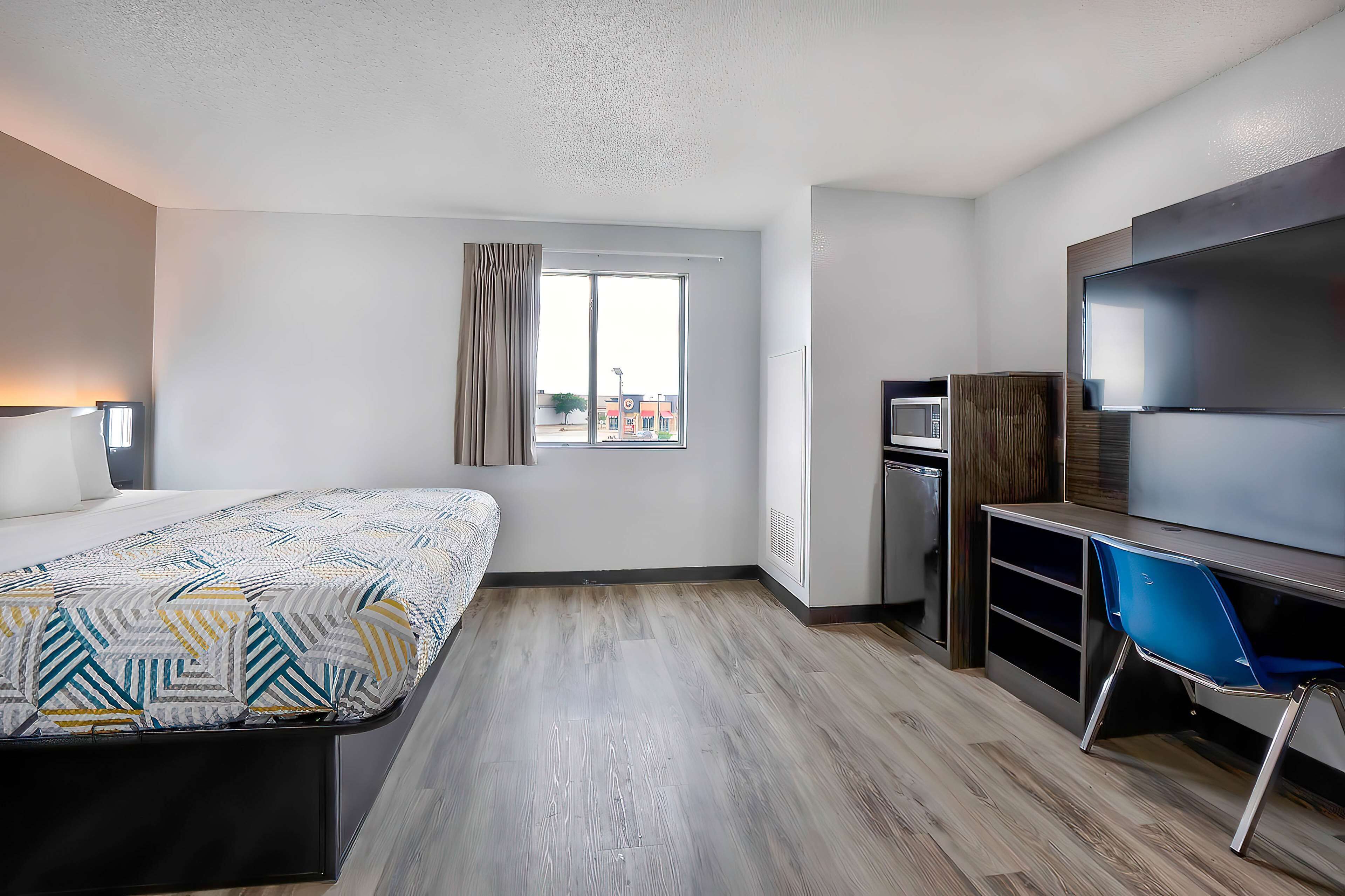 A hotel room with a bed, a desk, a chair, a TV, and a window.
