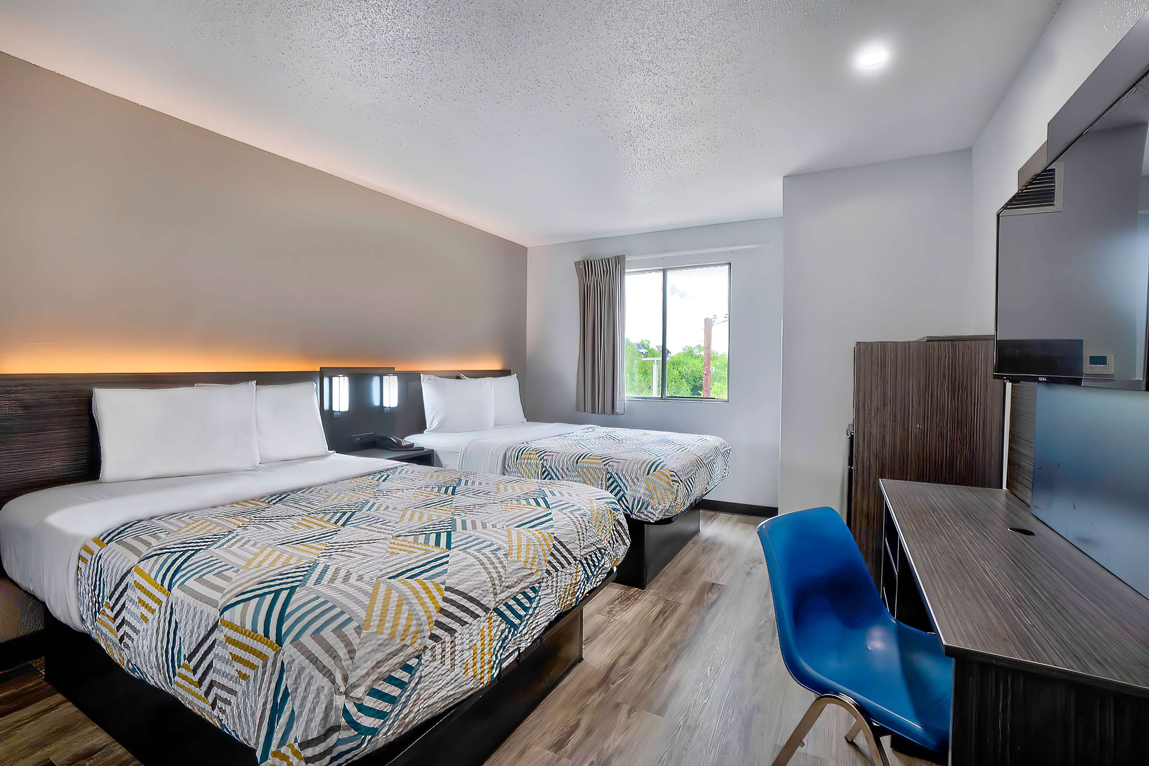 A hotel room with two beds, a desk, a chair, and a large window.