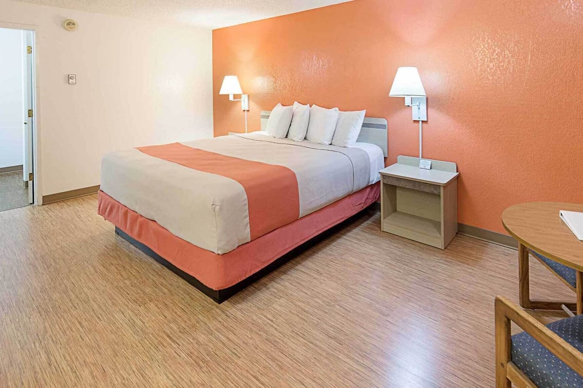 A hotel room with a bed, bedside lamps, a small table, and a chair.