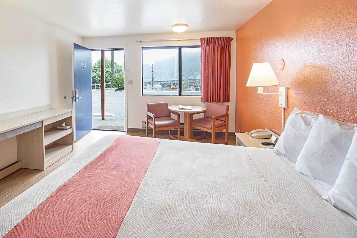 A hotel room with a bed, desk, chair, and a view through the window.