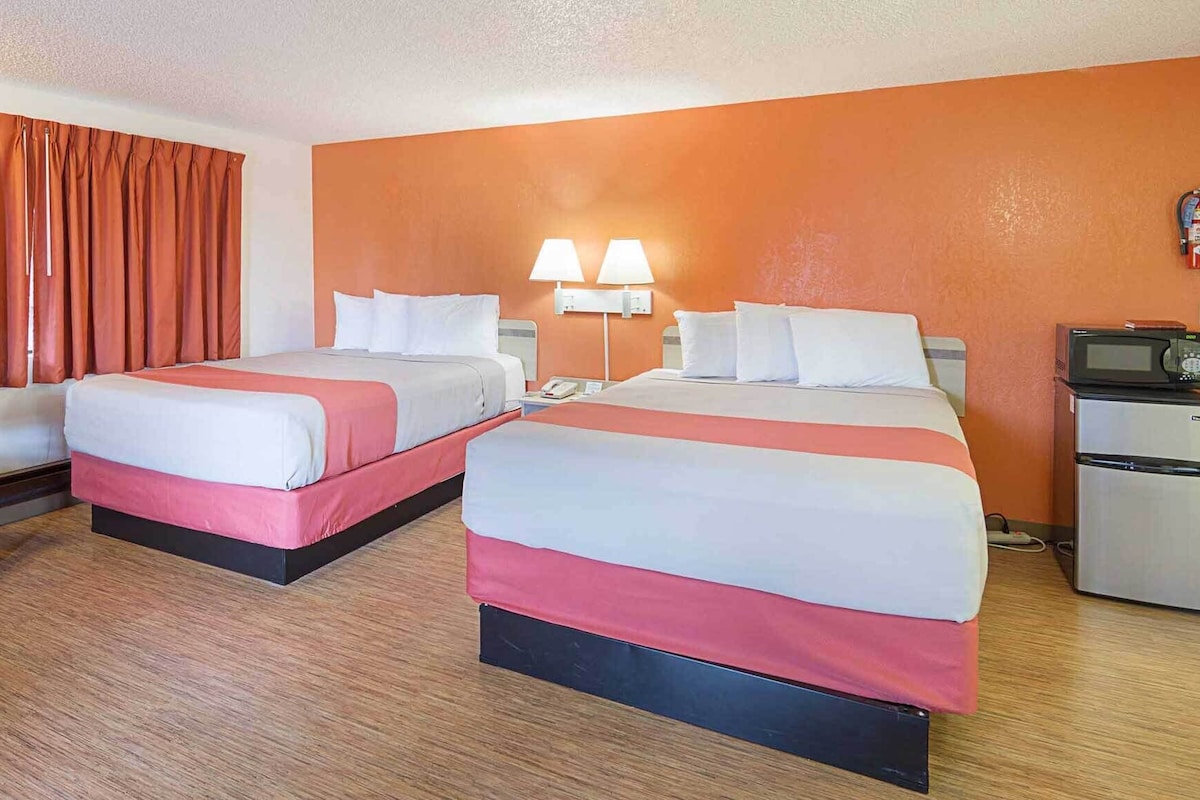 A hotel room with two beds, a desk, a chair, a microwave, and a refrigerator.
