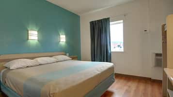Habitación de hotel con cama, dos lámparas de pared, ventana con cortinas y aire acondicionado instalado.
