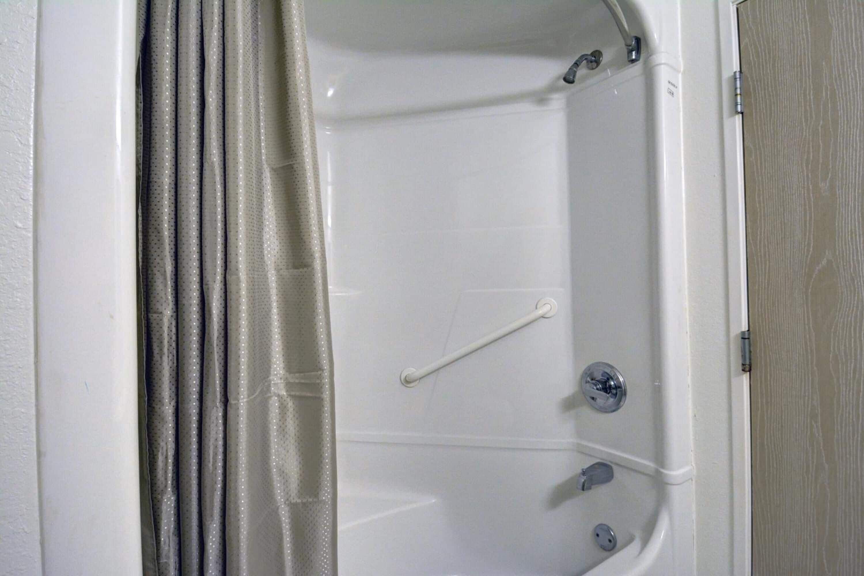 A white bathtub with a grab bar, a showerhead, and a faucet.