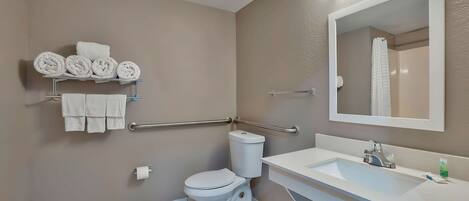 A modern bathroom with a toilet, sink, and handrails.