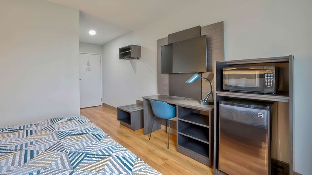 A modern bedroom with a bed, a desk, a chair, a TV, a microwave, and a mini-fridge. - Motel 6 Denison, TX (Denison)