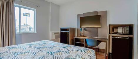 Una habitación de hotel con cama, escritorio, silla, televisor y microondas.