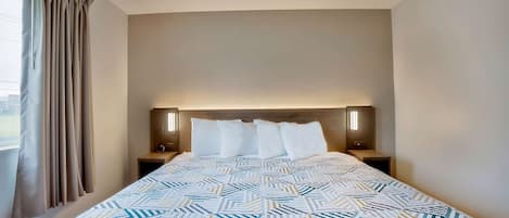 Quarto de hotel com uma cama grande, cabeceira com iluminação integrada e vista para o exterior pela janela.