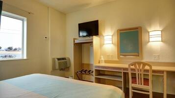 A hotel room with a bed, a desk with a chair, a television, and a window.