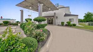 Ein moderner Hotel Eingangsbereich mit überdachtem Zugang, einem Parkplatz und gepflegter Bepflanzung.