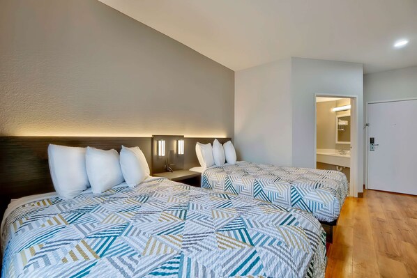 Ein Hotelzimmer mit zwei Betten, einem Holzkopfteil, einem Nachttisch und einem begehbaren Kleiderschrank.