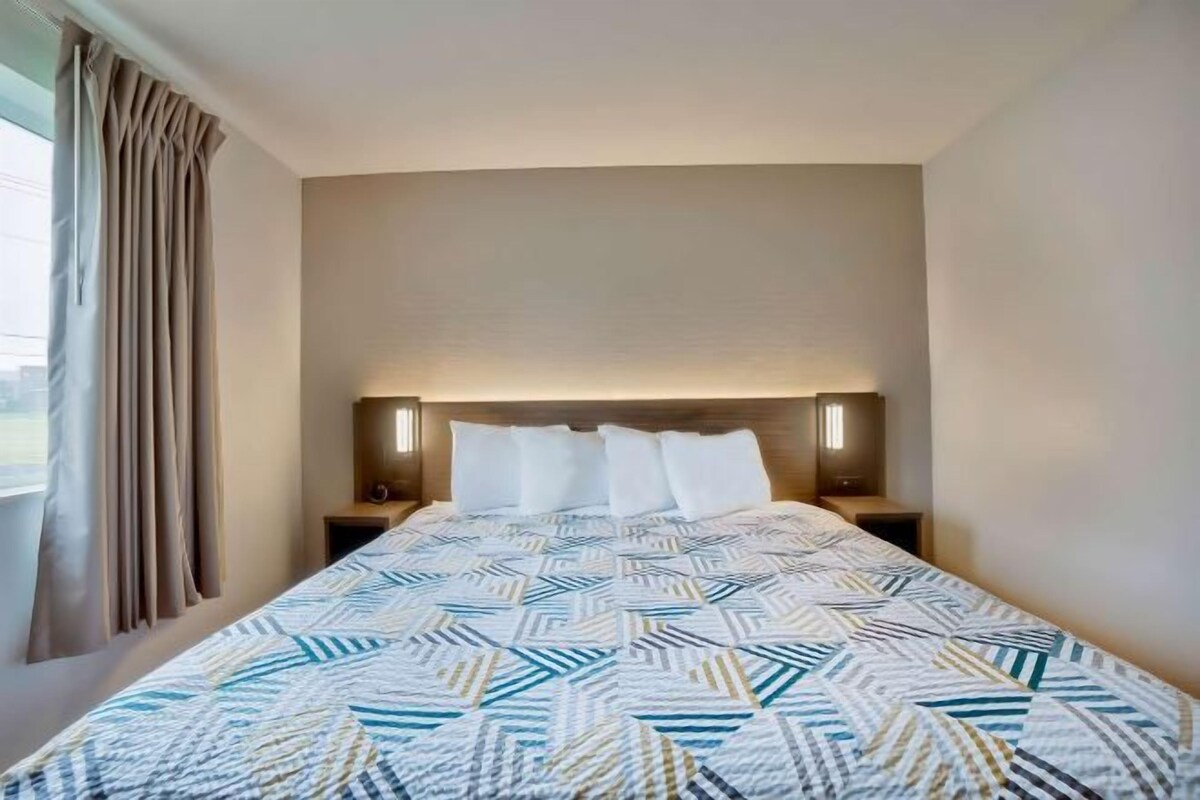 A hotel room with a large bed, beige walls, and a window with curtains.
