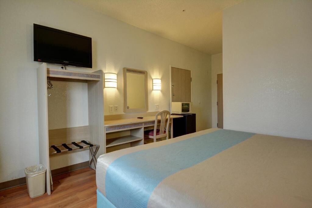 A hotel room with a bed, a desk, a chair, a television, a mirror, and a wardrobe.