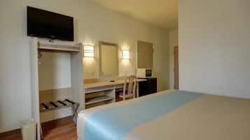 A hotel room with a bed, a desk, a chair, a television, a mirror, and a wardrobe.