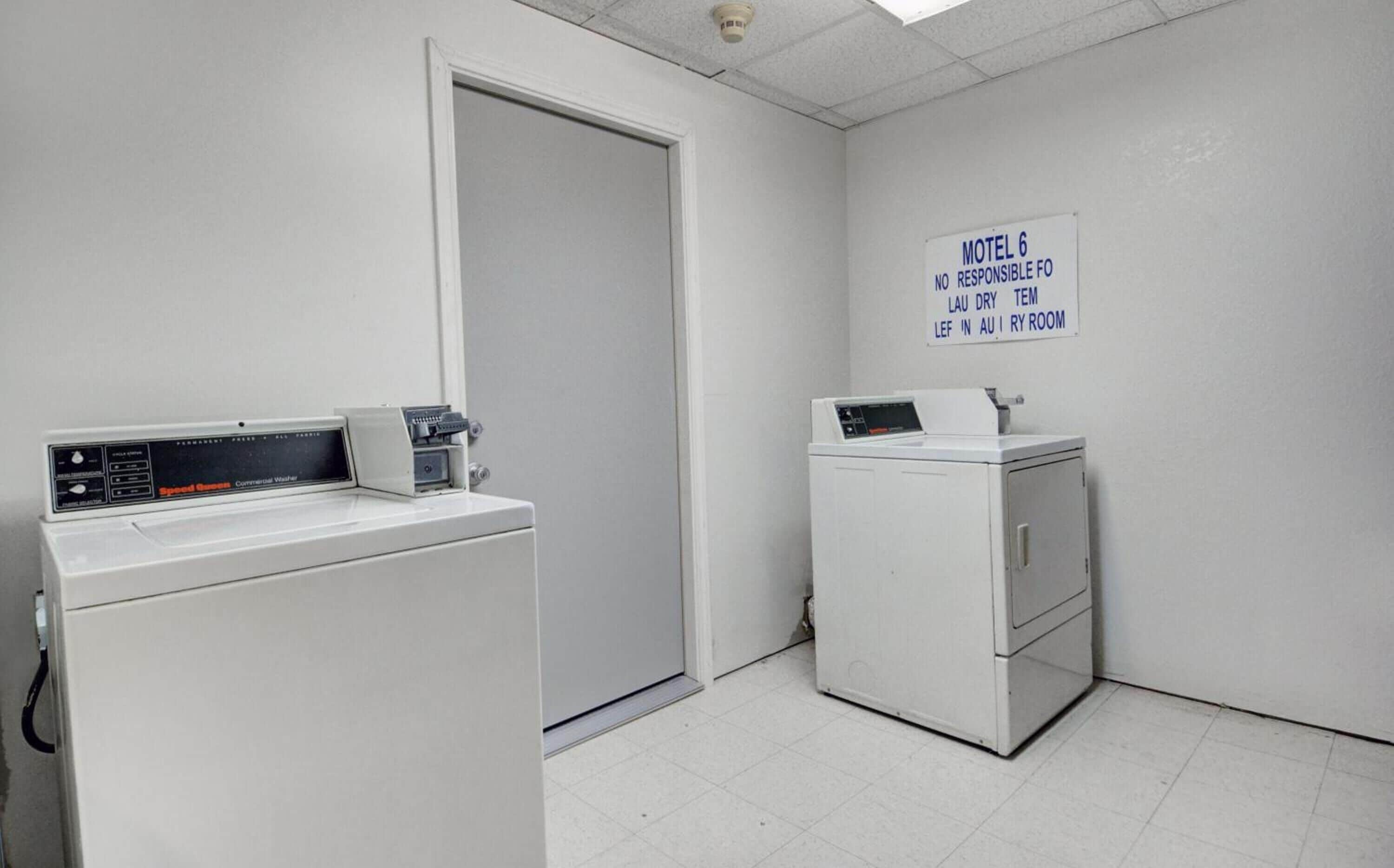 A laundry room with two washers and dryers, a sign indicating 'Motel 6 No Responsible FO Lau Dry Tem Left in Dry Room'.