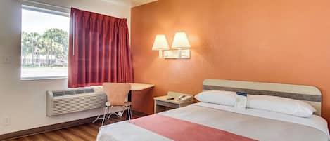 Habitación de hotel con cama, escritorio, silla, mesita de noche y ventana con cortinas.