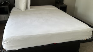 Una habitación de hotel moderna con una cama grande, dos mesitas de noche, una lámpara de pared y un pequeño tocador.