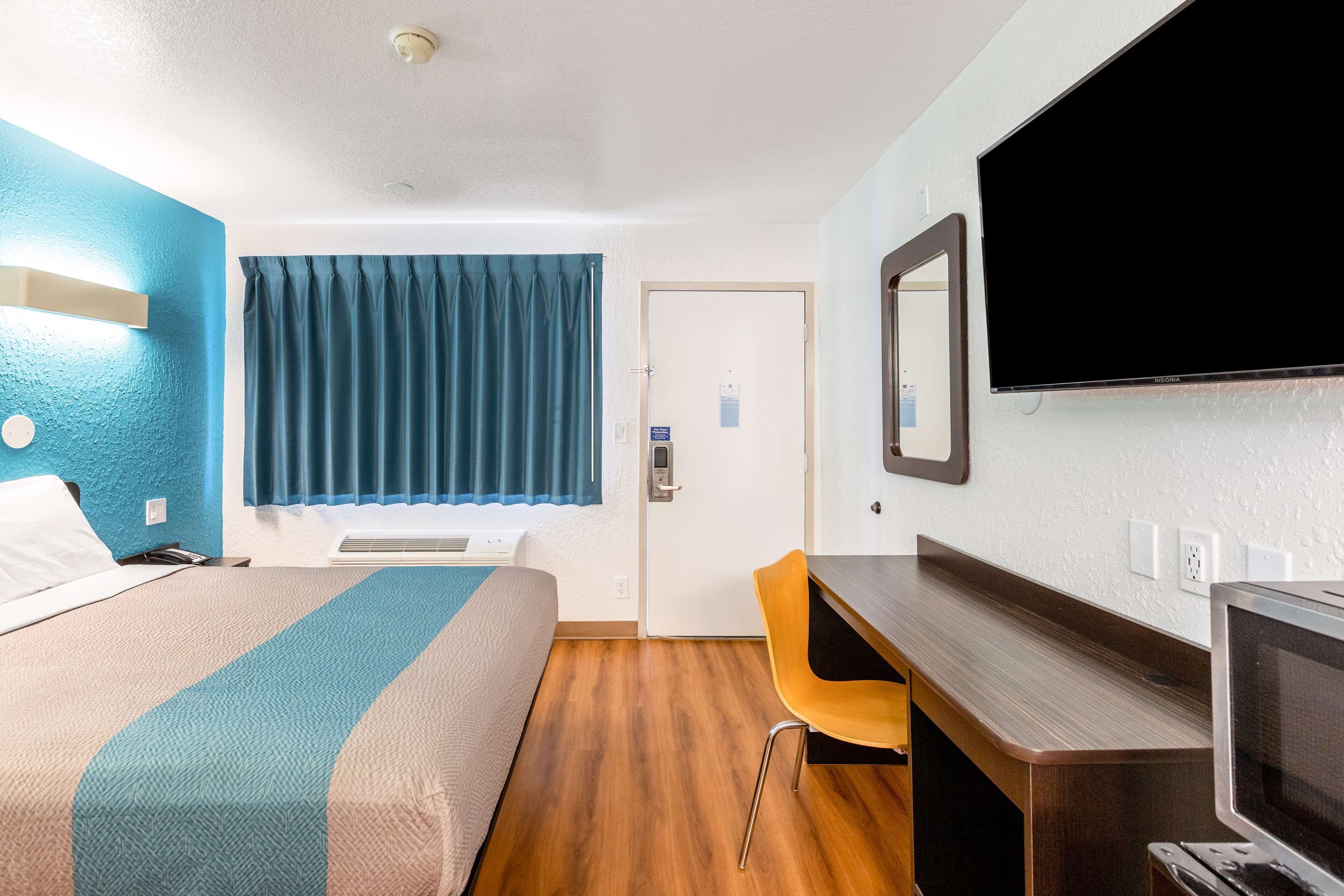 A hotel room with a bed, a desk, a chair, a television, and a window with curtains.