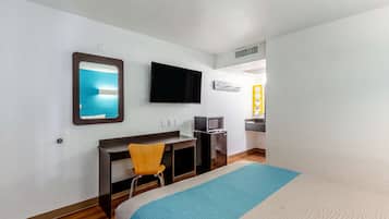 A hotel room with a bed, a desk, a chair, a TV, and a kitchenette.