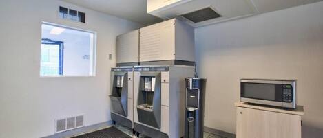 A commercial kitchen with three ice cube dispensers, a microwave, and a water dispenser.