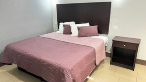 A neatly made bed with a headboard, a bedside table, and a wall-mounted light fixture. - Xpress Inn & Extended Stays (Marshall)