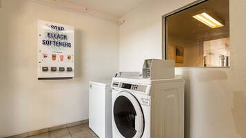 A laundry area with a washing machine, dryer, and a sign advertising soap, bleach, and softeners.