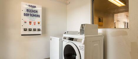 A laundry area with a washing machine, dryer, and a sign advertising soap, bleach, and softeners.