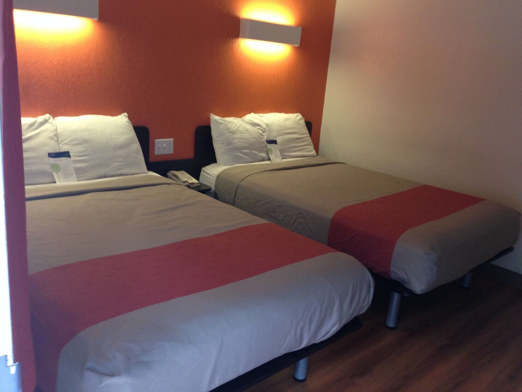 Dos camas individuales con ropa de cama roja y blanca, una mesita de noche con teléfono, y una lámpara fijada a la pared.