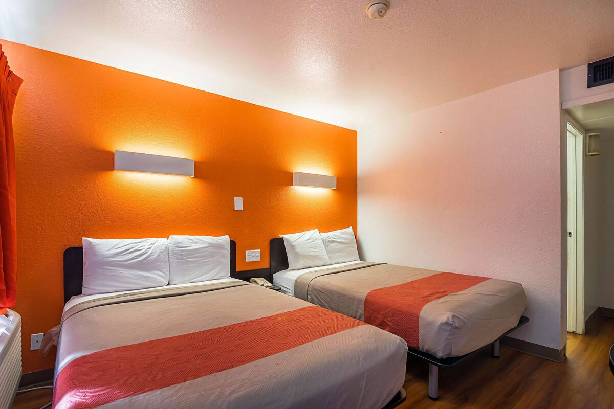 Una habitación de hotel con dos camas, paredes anaranjadas y dos luces fijadas a la pared.