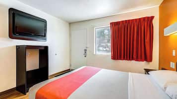 A hotel room with a bed, a television mounted on the wall, a wardrobe, a window with curtains, and a door.