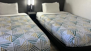 Two single beds with geometric patterned bedding, a bedside table with a phone, and a wall-mounted light fixture.