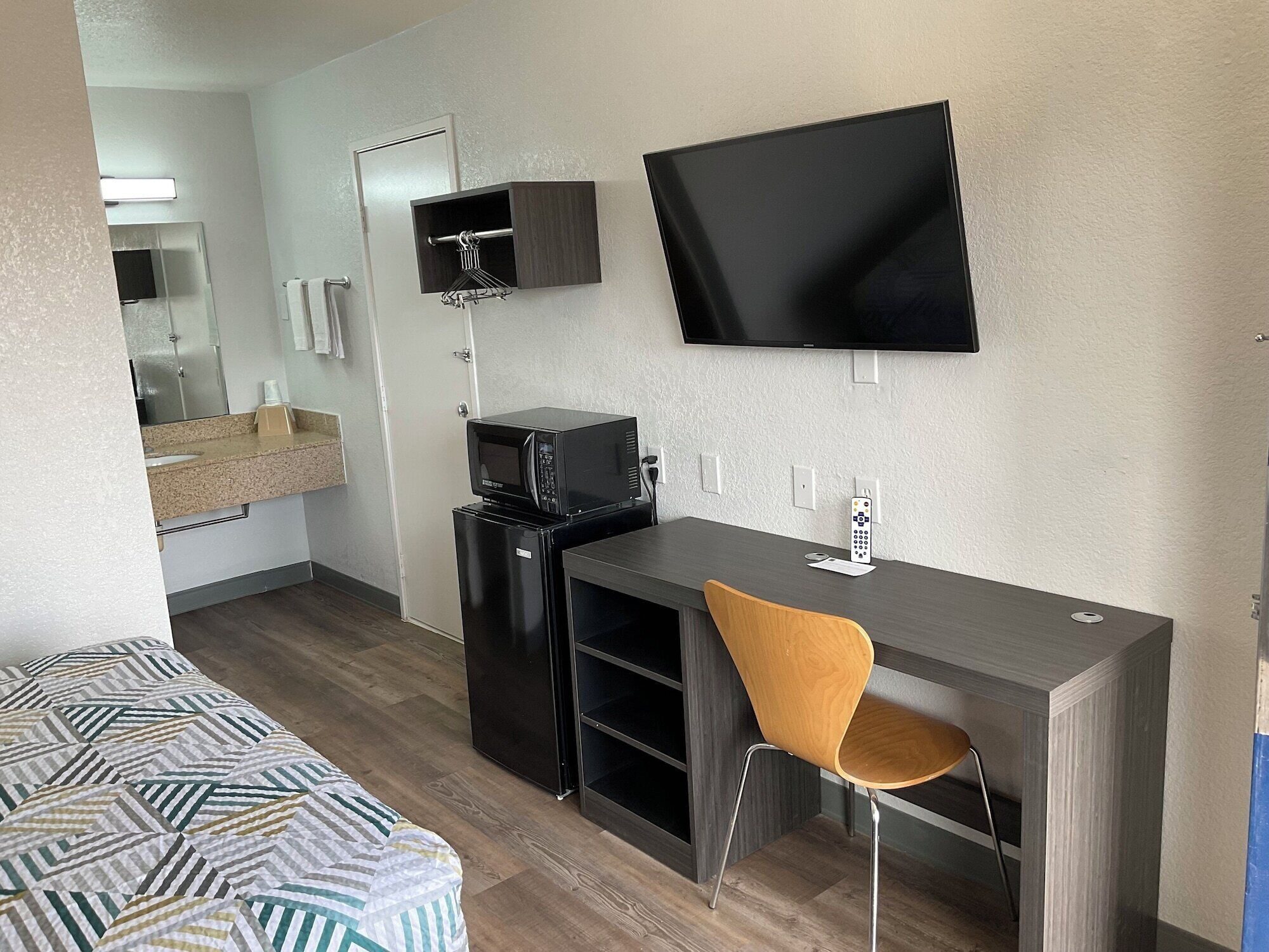 Habitación de hotel con cama, escritorio, silla, televisión, microondas y refrigerador pequeño.