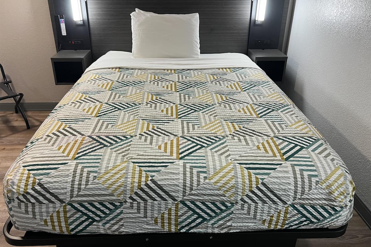 A neatly made bed with a patterned bedspread, two bedside lamps, and a headboard.
