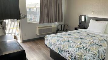 A hotel room with a bed, a desk, a chair, a TV, a window with curtains, and a radiator.