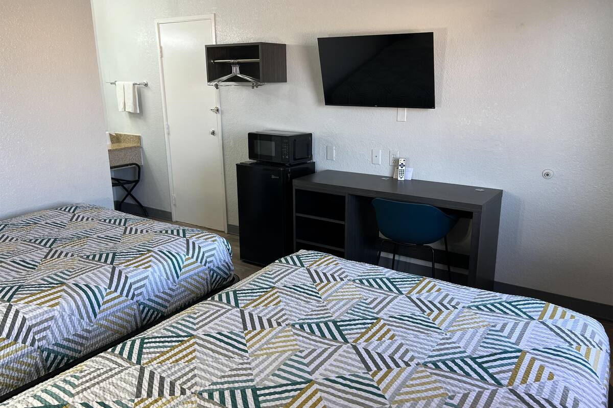 A hotel room with two beds, a desk, a chair, a TV, and a microwave.