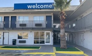 A building with a 'Welcome' sign, a palm tree, and a parking lot with marked spaces. - Motel 6 Odessa, TX (Odessa)