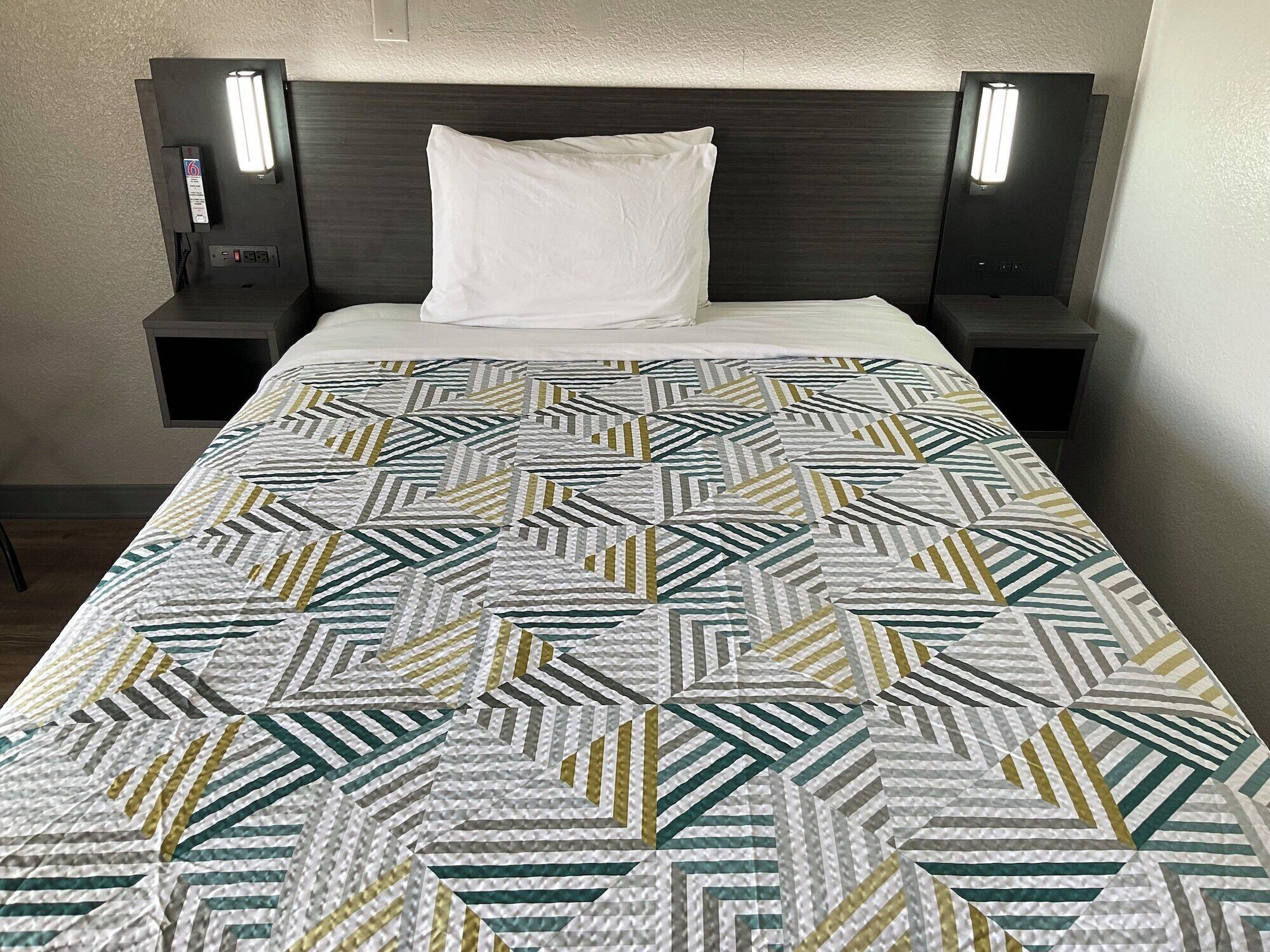 A bed with a patterned quilt, a white pillow, and two bedside tables with lamps.