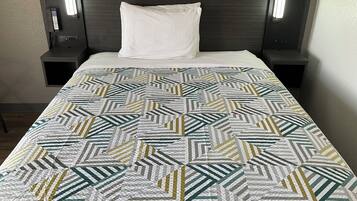 A bed with a patterned quilt, a white pillow, and two bedside tables with lamps.