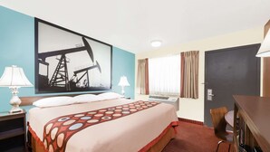 A hotel room with a large bed, two bedside tables with lamps, a desk with a chair, a window with curtains, and a door. - Super 8 by Wyndham Midwest City OK (Midwest City)