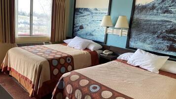 Quarto de hotel com duas camas, uma janela grande com cortinas, um quadro na parede e um abajur na mesa de cabeceira.