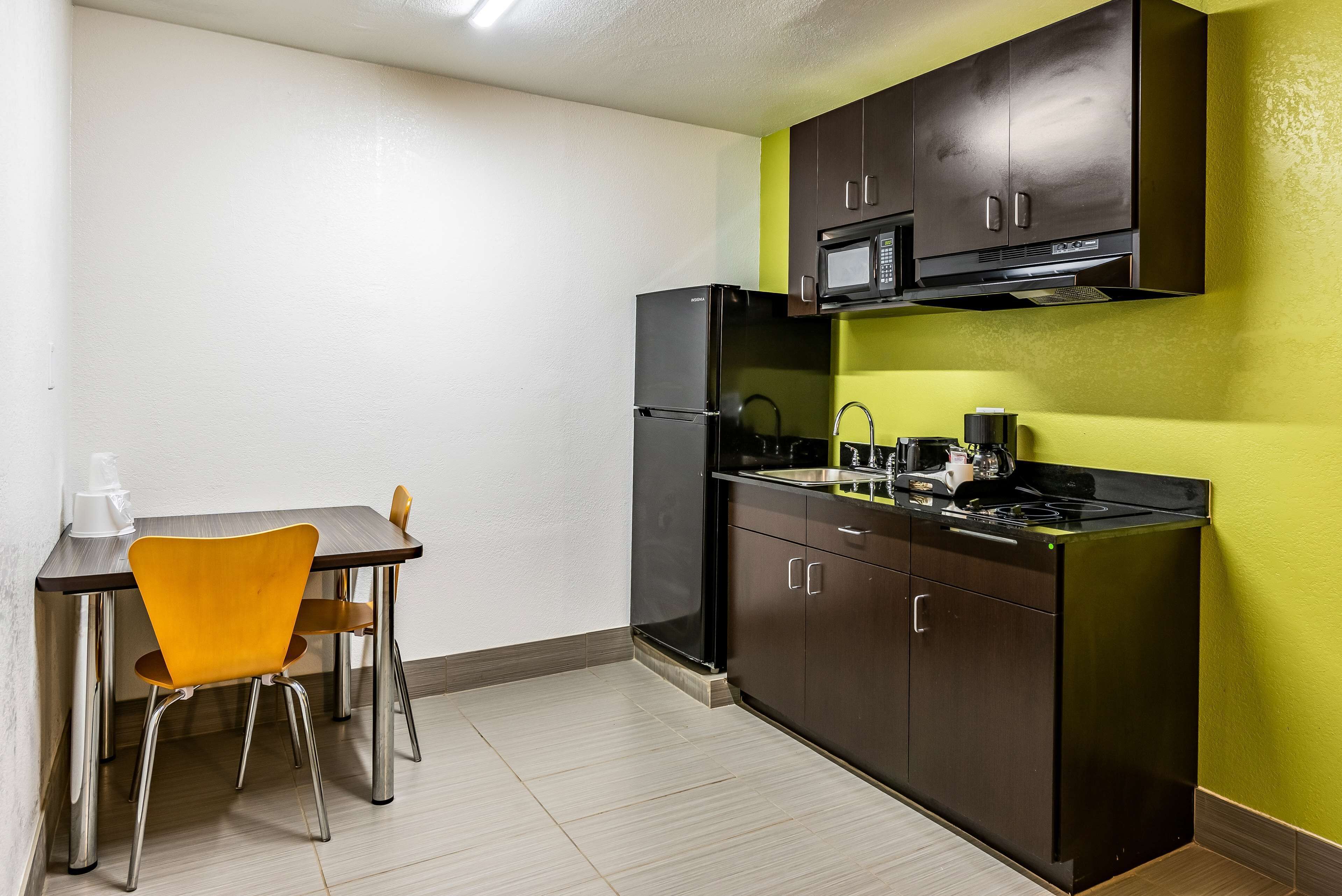 Une cuisine compacte équipée d’un réfrigérateur, d’un four à micro-ondes et d’une cuisinière, une table à manger avec deux chaises et un mur jaune.
