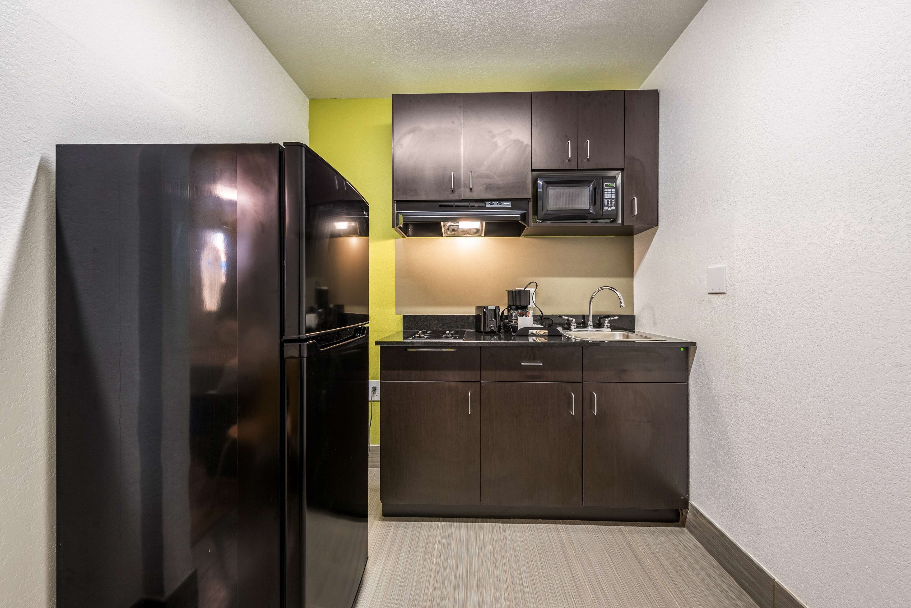 A compact kitchen with dark cabinetry, a stainless steel refrigerator, a microwave, and a sink.