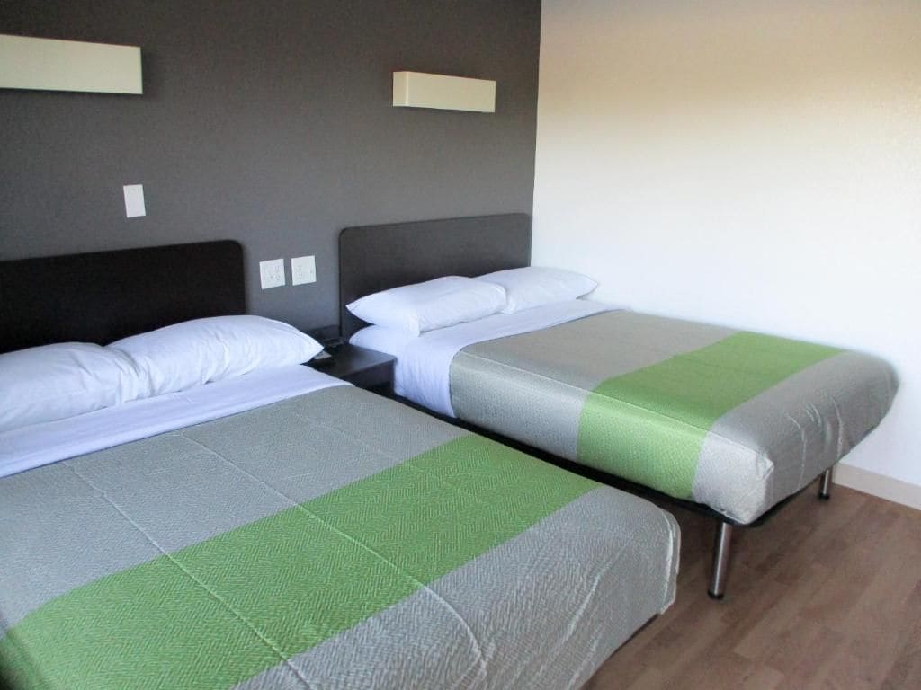 Ein Hotelzimmer mit zwei Betten, jeweils mit einer grauen und grünen Tagesdecke sowie einem dunklen Kopfteil.