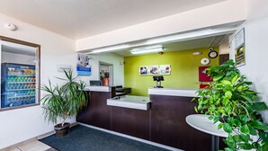 A reception desk with a green wall, a potted plant, and a Coca-Cola refrigerator. - Studio 6 Monroe, LA - Hwy 165 (Monroe)